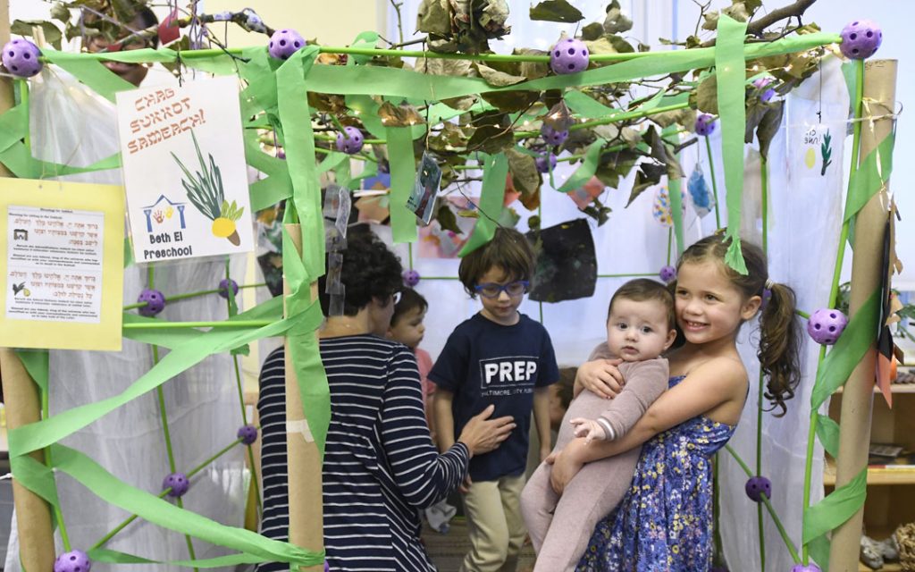 Clara Wexler, 4, holds her four-mounth-old sister Lia in a sukkah during the "Sukkot Under the Stars" event at Beth El preschool in Federal Hill. (Photo by Steve Ruark)