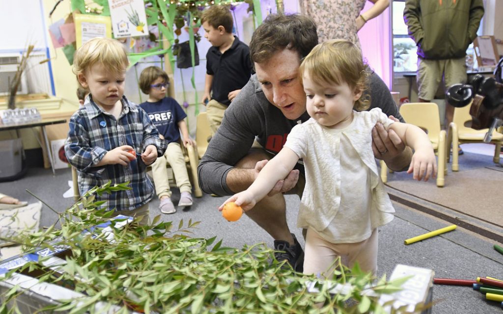 Mike Rubin helps his 18-month-old daughter Ida place citrus in a small sukkah during the "Sukkot Under the Stars" event at Beth El preschool in Federal Hill. (Photo by Steve Ruark)