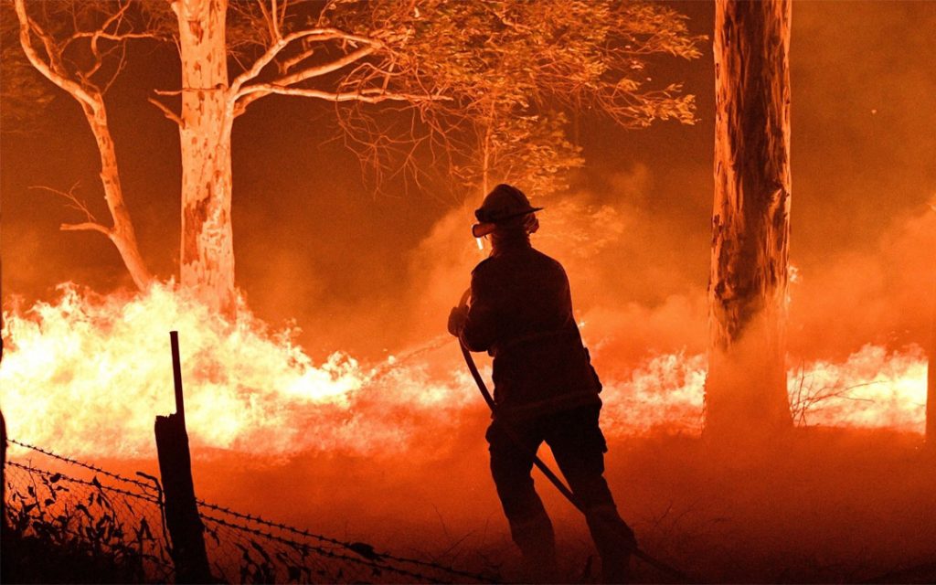 A firefighter in Australia hoses down trees to protect nearby homes from bush fires near the town of Nowra in the state of New South Wales on Dec. 31, 2019 as the fires led to the evcacuation of popular tourist areas in the state. (Saeed Kahn/AFP via Getty Images)