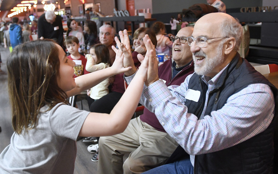 Gil Abramson, right, high-fives his granddaughter during the Macks Center for Jewish Education's Saba-ba: Grandparents on the Go launch party at AMF Pikesville Lanes (Photo by Steve Ruark)