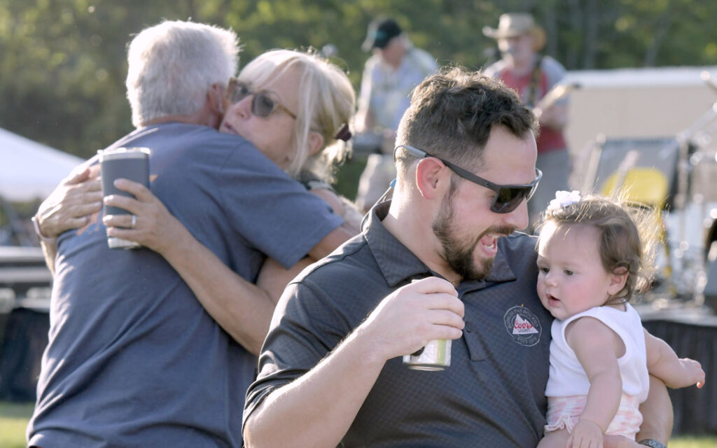 From left, Sheldon Strauss, of Lutherville, hugs Sue Markowitz, of Pikesville, as Mike Tompakov, of Sykesville, dances with his 7-month-old daughter, Stella, during Chizuk Amuno Congregation’s SummerFest.