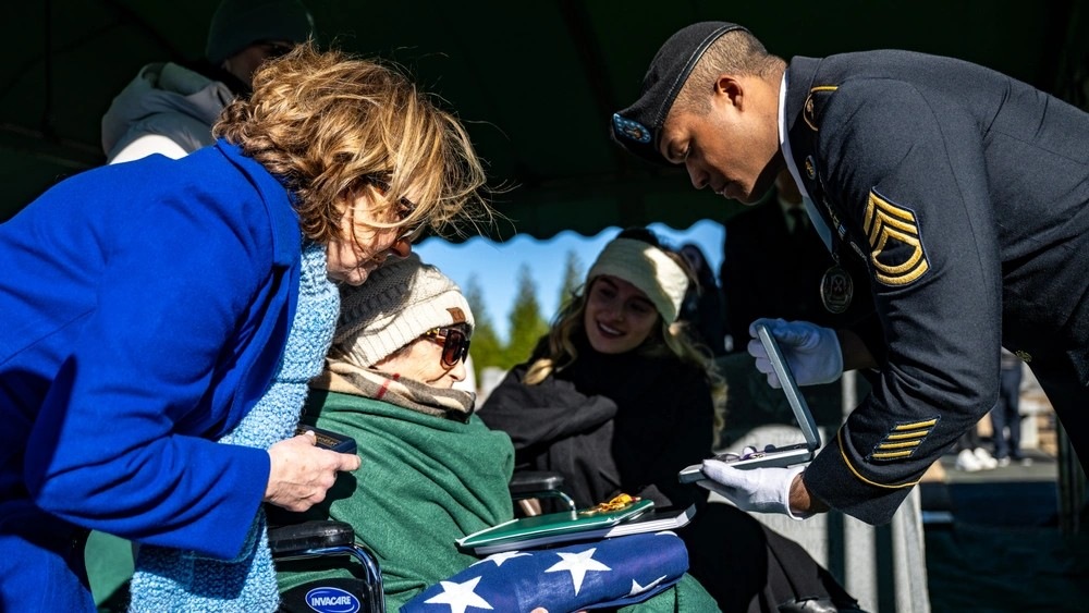 A U.S. Honor Guard presents a flag to Carol Fine, sister of Lt. Morton Sher.